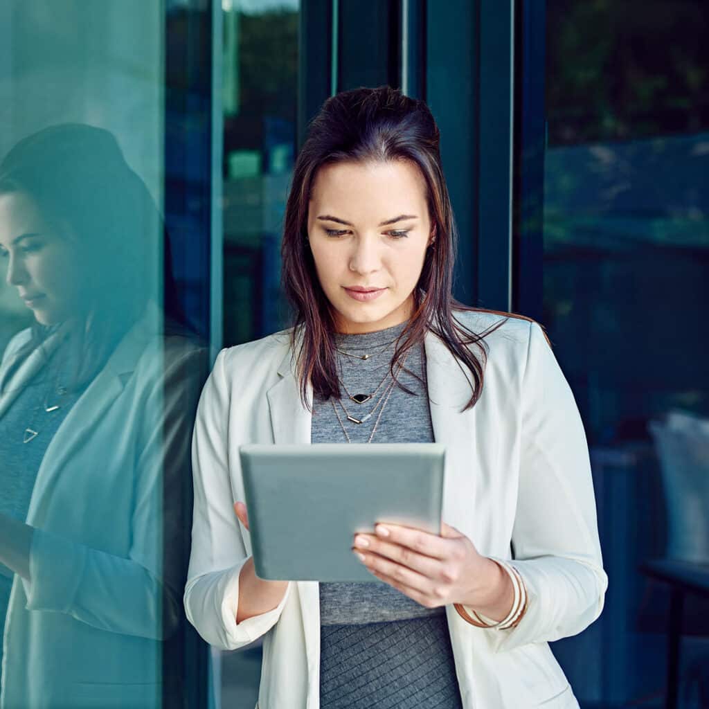 Woman reading news on a tablet while standing outside office.