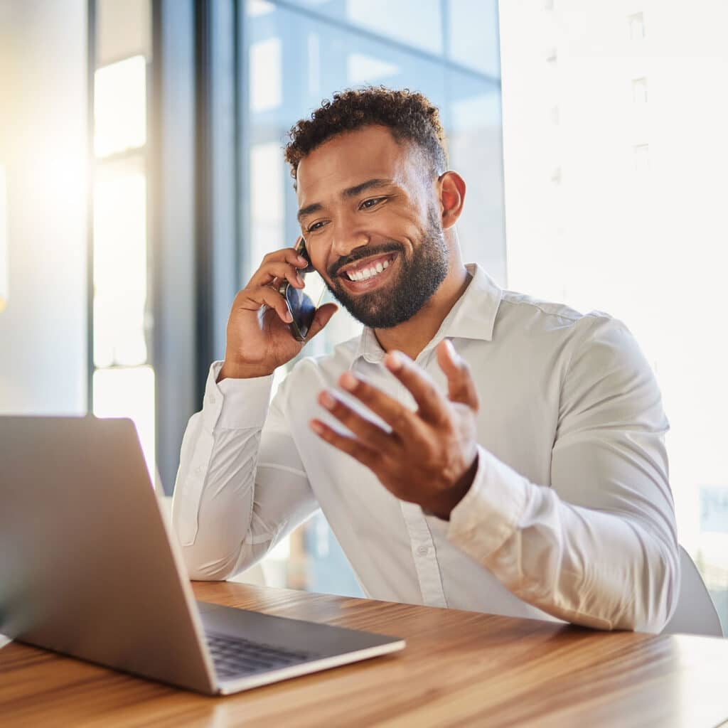 Male professional sitting at desk in office talking on mobile phone.